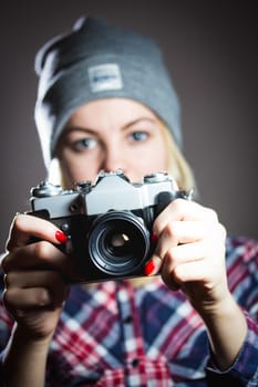 Portrait of hipster girl taking picture with retro camera wearing checkered shirt and winter hat.