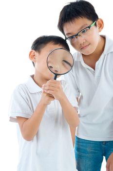 A little chinese boy and his brother peers at the camera through a magnifying glass, isolated on white background