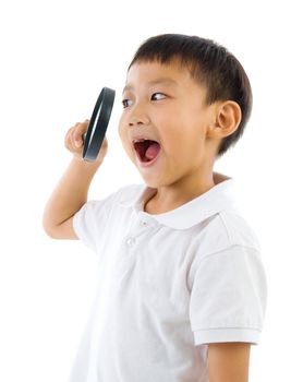 A little chinese boy peers at the camera through a magnifying glass, isolated on white background