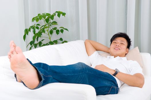 Asian guy resting at home. Asian handsome man relaxed and lying on sofa indoor.