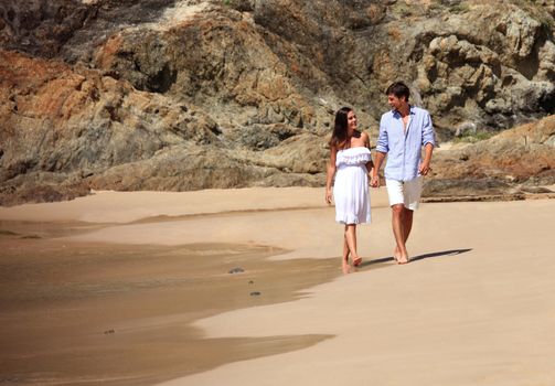 Cheerful couple walking on beach on rock background