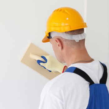 Male plasterer in uniform polishing the wall