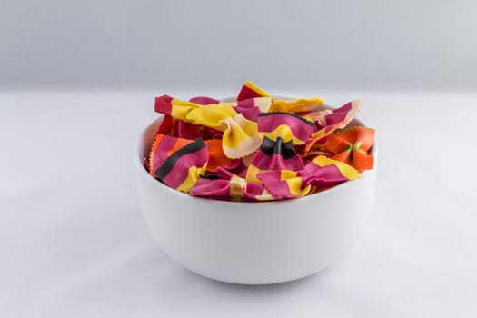 Bowl of colourful pasta bows against a white background