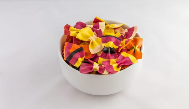 Bowl of colourful pasta bows against a white background