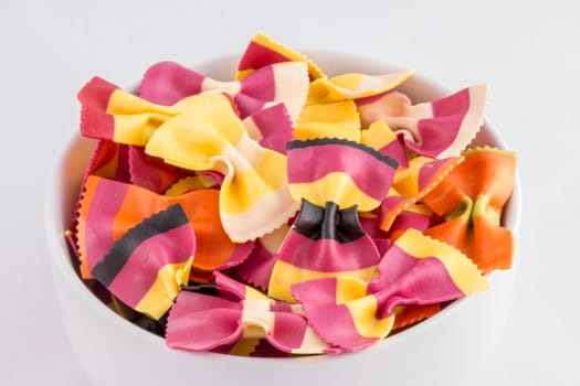 Bowl of colourful pasta bows against a white background