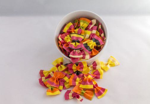 overflowing bowl of colourful pasta bows against a white background