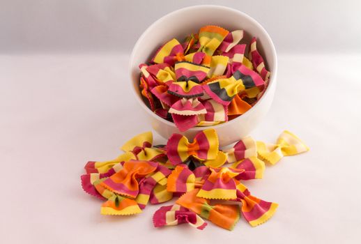 overflowing bowl of colourful pasta bows against a white background