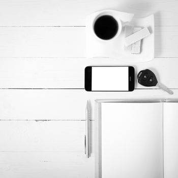 coffee cup with wafer,phone,car key,notebook on white wood background black and white color