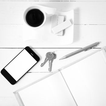 coffee cup with wafer,phone,key,notebook on white wood background black and white color