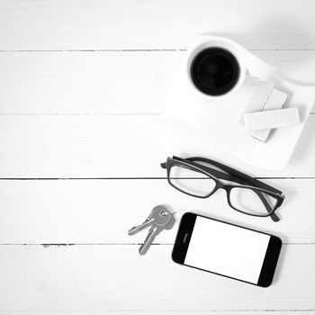 coffee cup with wafer,phone,key,eyeglasses on white wood background black and white color