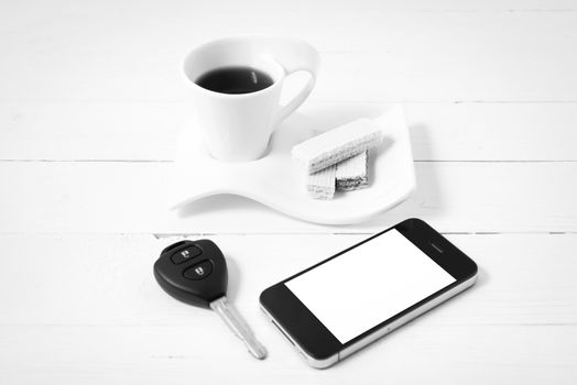 coffee cup with wafer,phone,car key on white wood background black and white color