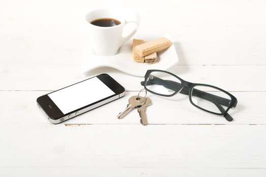 coffee cup with wafer,phone,key,eyeglasses on white wood background