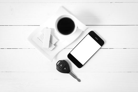 coffee cup with wafer,phone,car key on white wood background black and white color