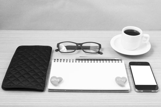 office desk : coffee with phone,notepad,eyeglasses,wallet,heart on wood background black and white color