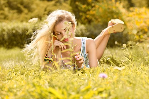 Beauty playful woman relax in summer garden dreaming on grass, people, outdoors, bokeh. Attractive happy blonde girl enjoying nature, harmony on meadow, lifestyle.Sunny day, forest, flowers, copyspace