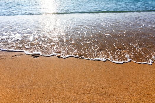 Soft wave of the sea washing foot marks from the sandy beach