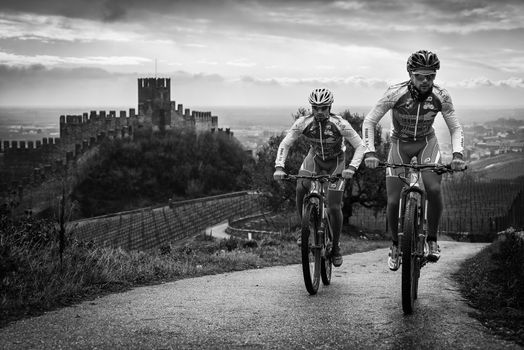 Soave, Italy - March 27, 2016: Cyclists train after a storm on the hills surrounding the castle of Soave.