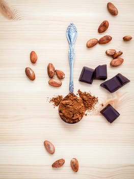 Brown chocolate powder in spoon , Roasted cocoa beans and dark chocolate setup on wooden background.