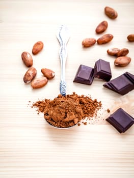 Brown chocolate powder in spoon , Roasted cocoa beans and dark chocolate setup on wooden background. Selective focus depth of field on chocolate powder.