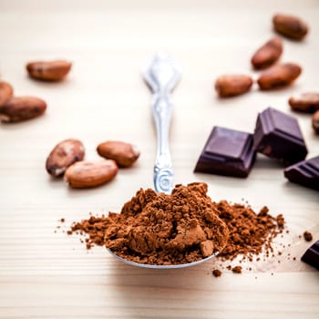 Brown chocolate powder in spoon , Roasted cocoa beans in the dry cocoa pod fruit and dark chocolate setup on wooden background.