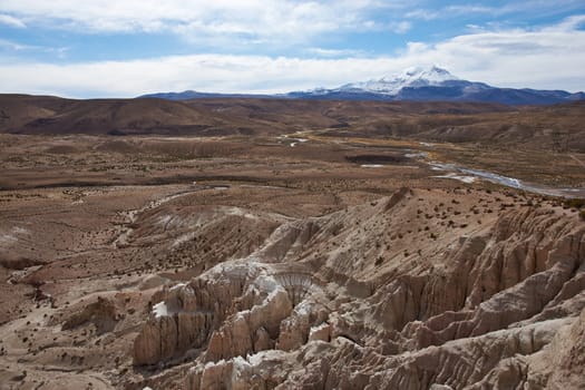 Eroded rock formations at the head of a river valley feeding the River Lauca high up on the Altiplano of northern Chile in Lauca National Park. In the background is the snow capped active Guallatiri volcano (6063 m).