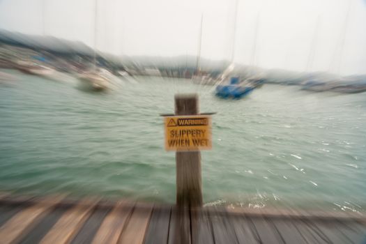 Warning og danger near harbor Slippery when wet sign in zoom blur effect