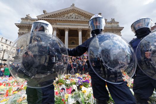 BELGIUM, Brussels : Belgian policemen stand guard as people gather at the makeshift memorial on the Place de la Bourse Square, in Brussels, on March 27, 2016 to pay tribute to the victims of the Brussels terror attacks which killed 31 people and injured over 300.Riot police fired water cannon on March 27, 2016 at far-right football hooligans who invaded a square in the Belgian capital that has become a memorial to the victims of the Brussels attacks, an AFP journalist said. Police took action after about 200 black-clad hooligans shouting nationalist and anti-immigrant slogans moved in on the Place de la Bourse where people were gathering in a show of solidarity with the victims. 