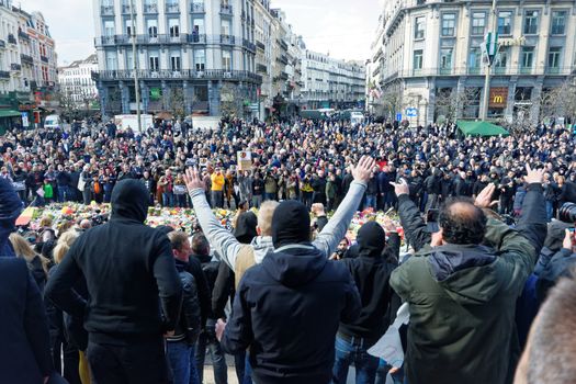 BELGIUM, Brussels : Far-right football hooligans chant slogans as they stand in the square outside the stock exchange in Brussels on March 27, 2016 an area which has become an unofficial shrine to victims of the March 22, terror attacks claimed by the Islamic State (IS) group in which 31 people were killed and over 300 injured.Police fired water a cannon at far-right football hooligans who invaded a square in the Belgian capital that has become a memorial to the victims of the Brussels attacks, an AFP journalist said. Police took action after about 200 black-clad hooligans shouting nationalist and anti-immigrant slogans moved in on the Place de la Bourse where people were gathering in a show of solidarity with the victims.
