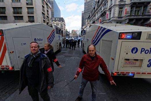 BELGIUM, Brussels : Belgian policemen stand guard as people gather at the makeshift memorial on the Place de la Bourse Square, in Brussels, on March 27, 2016 to pay tribute to the victims of the Brussels terror attacks which killed 31 people and injured over 300.Riot police fired water cannon on March 27, 2016 at far-right football hooligans who invaded a square in the Belgian capital that has become a memorial to the victims of the Brussels attacks, an AFP journalist said. Police took action after about 200 black-clad hooligans shouting nationalist and anti-immigrant slogans moved in on the Place de la Bourse where people were gathering in a show of solidarity with the victims. 