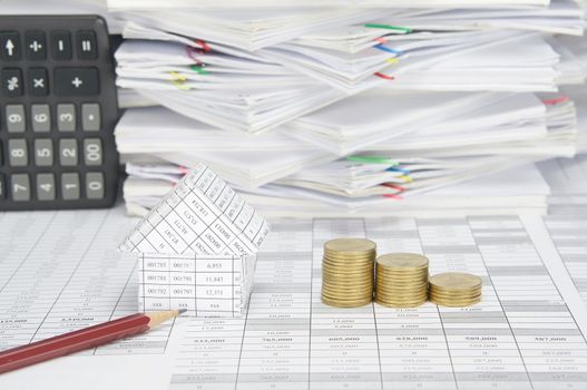 Close up house and brown pencil with step pile of gold coins on finance account have calculator place vertical and overload of paperwork with colorful paperclip as background.
