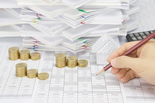 Man is auditing account by pencil with step pile of gold coins on the statement finance account have house with calculator and overload of paperwork with colorful paperclip as background.