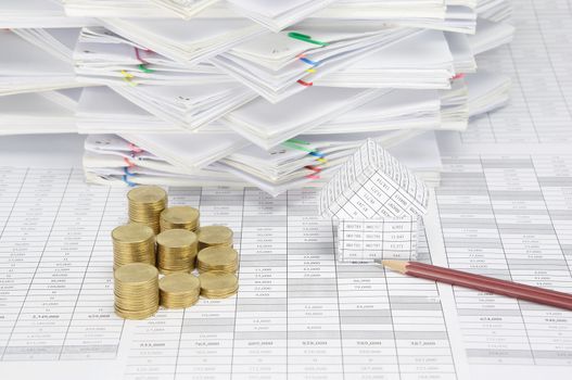 Brown pencil and house with step pile of gold coins on finance account have overload of paperwork with colorful paperclip as background.