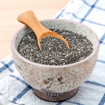 Nutritious chia seeds in ceramic bowl with wooden spoon for diet food ingredients.