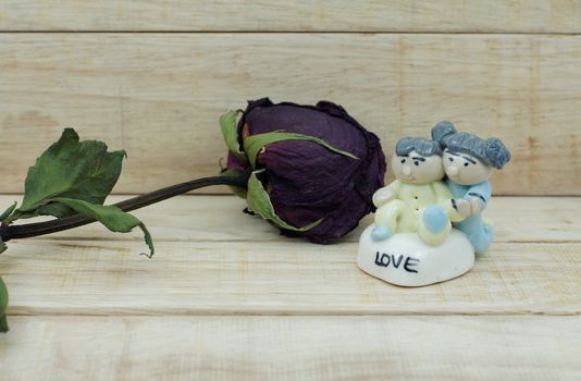 Dry roses and ceramic doll on wood pattern background. Dry roses with boy and girl ceramic doll with love text on wood background.