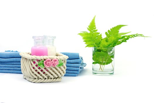 Shampoo and Shower gel put in ceramic basket on white background. Shampoo, Shower gel bottles with blue cloth and green leaves in a glass of water.