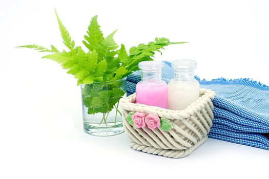 Shampoo and Shower gel put in ceramic basket on white background. Shampoo, Shower gel bottles with blue cloth and green leaves in a glass of water.