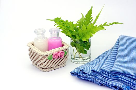 Shampoo and Shower gel put in ceramic basket on white background. Shampoo, Shower gel bottles with blue cloth and green leaves in a glass of water.