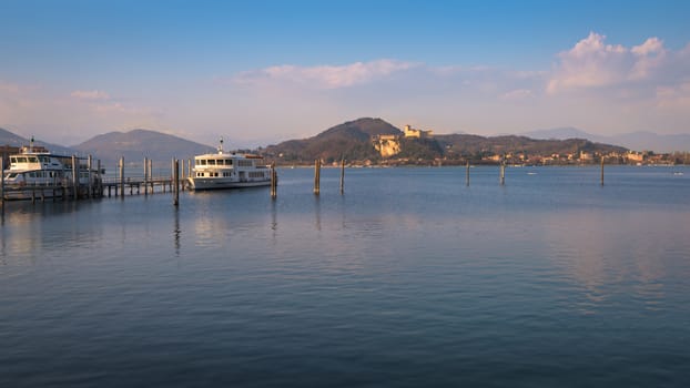 In the picture boats and yachts moored at the port of Arona, Maggiore Lake and in the background the fortress of Angera.