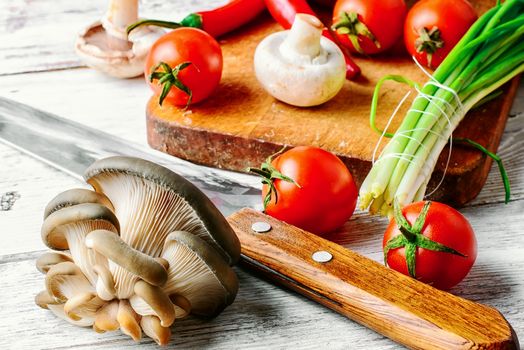 Fresh mushrooms,tomatoes,peppers and onions on a light wooden background