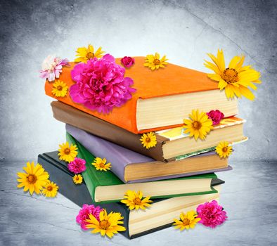 Pile of books with flowers on grey wall background, closeup