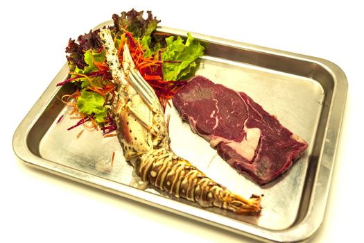 Set for surf and turf a fresh crude lobster and a juicy piece of a marble stake on a tray