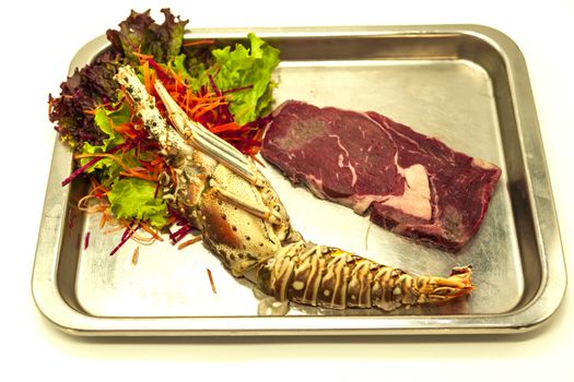 Set for surf and turf a fresh crude lobster and a juicy piece of a marble stake on a tray
