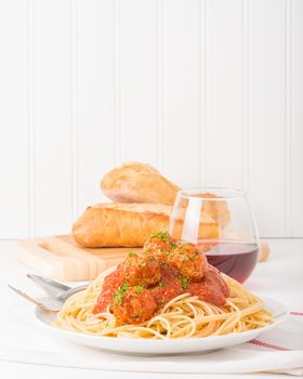 Plate of traditional Italian spaghetti and meatballs with bread and wine.