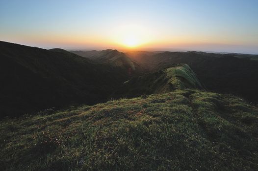 Path on top of green hill om light of orange sunset