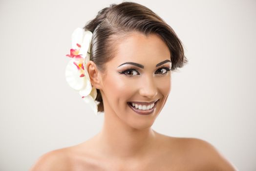 Portrait of a attractive young woman with nice make up and white orchid in her hair posing in a studio. Looking at camera.