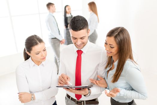 Three smiling young colleagues discussing in front their business team.