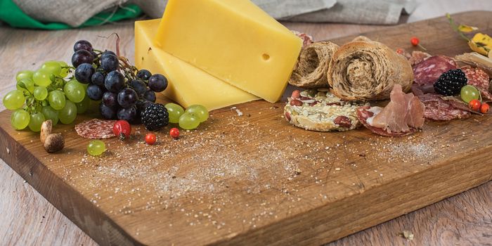 Fresh grapes, cheese bacon berries and salami on wooden table