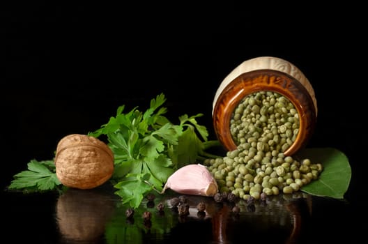Peas, parsley and spices on a black background, with reflection on the polished wooden surface.