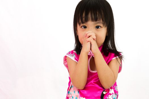 Chinese little girl wearing Cheongsam praying in plain white background.