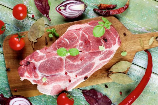 Perfect Raw Pork Neck with Spices, Ripe Tomatoes, Red Onion and Fresh Basil Leaves closeup on Wooden Cutting Board. Top View